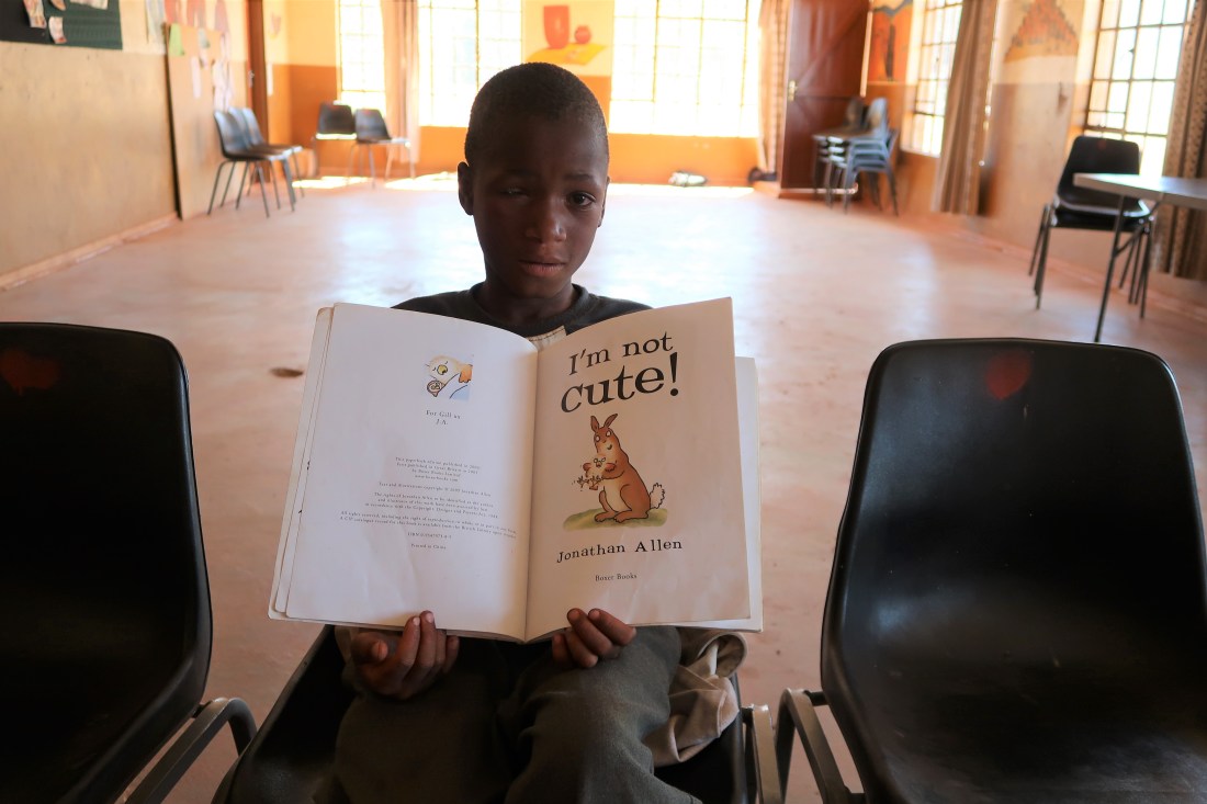 a young boy poses shyly with his favorite book, called "I'm Not Cute"