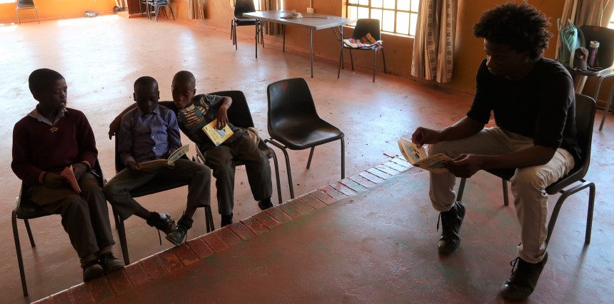 three boys read while being supervised by a man