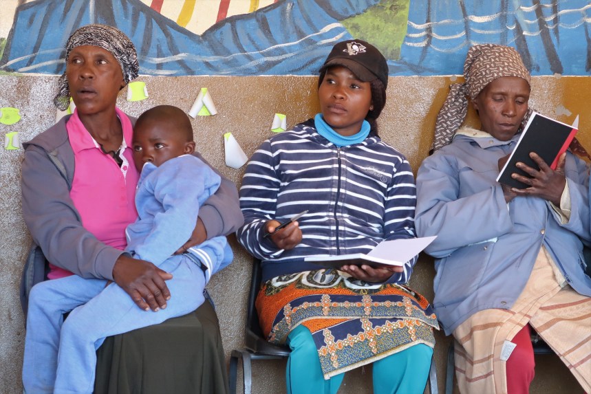 a mother holds her young son, while two other women are taking notes on the discussion at the Malealea Development Trust's HIV/AIDs support group discussion in Lesotho, Southern Africa