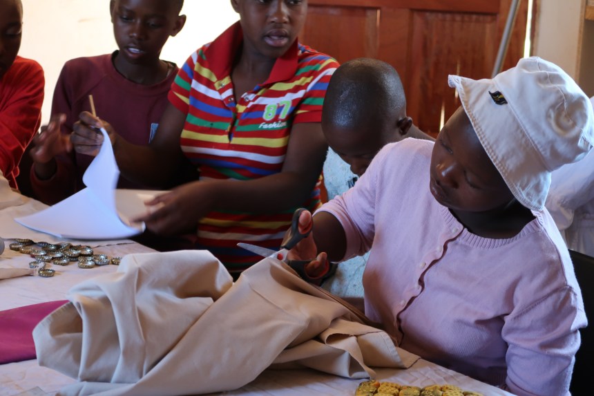 a young girl cuts fabric in the Malealea Development Trust's Young Women's Support Group, making a table mat and sanitary pad