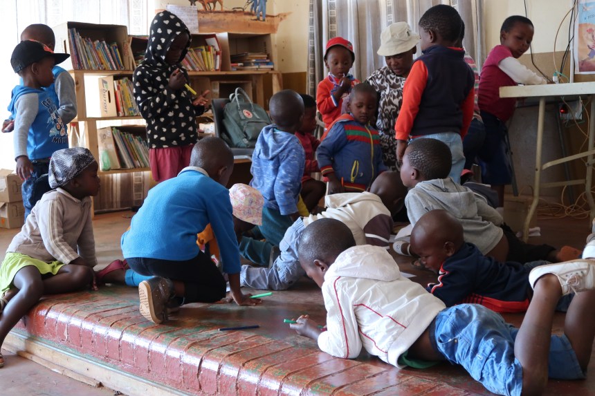 a group of children lie on the floor coloring at the Malealea Development Trust's Children's Day in Lesotho, Southern Africa