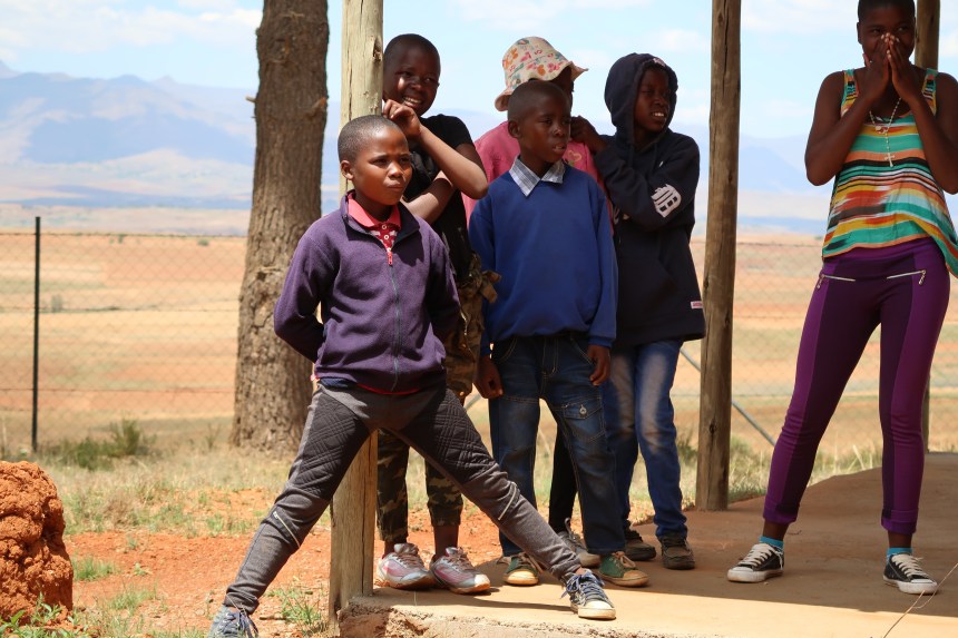 children standing outside in front of mountains listening to the Children's Day discussion. one of the girls is laughing at something funny that has just been brought up.