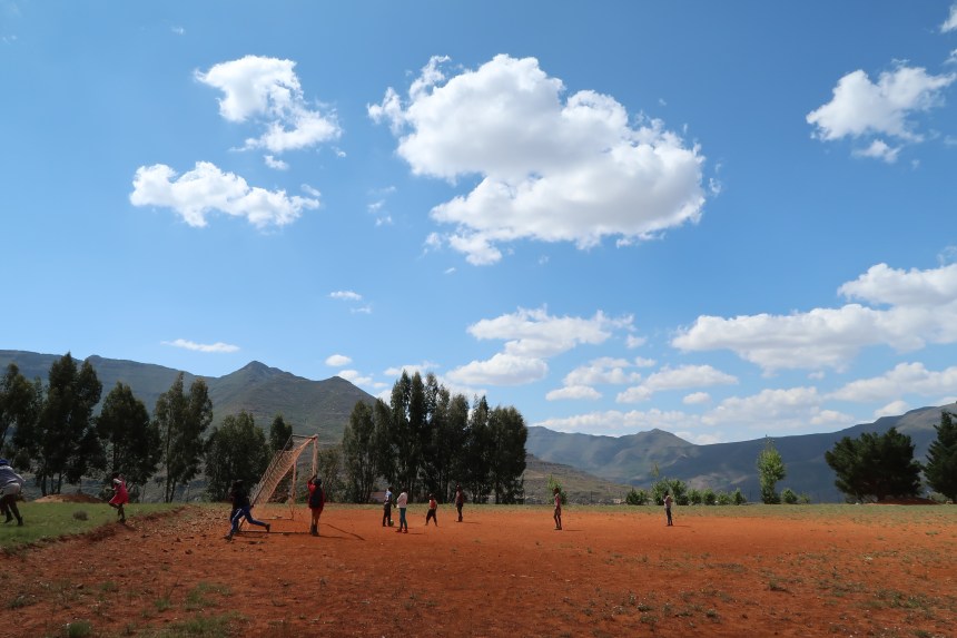 a group of children play soccer under a brilliant blue sky, surrounded by green mountains in Malealea, Lesotho, Southern Africa