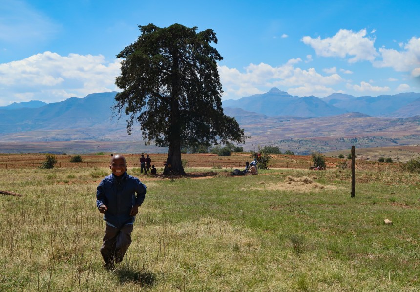 a smiling boy runs across the schoolyard, mountains in the background, in Malealea, Lesotho, Southern Africa, photo by Kelly Benning