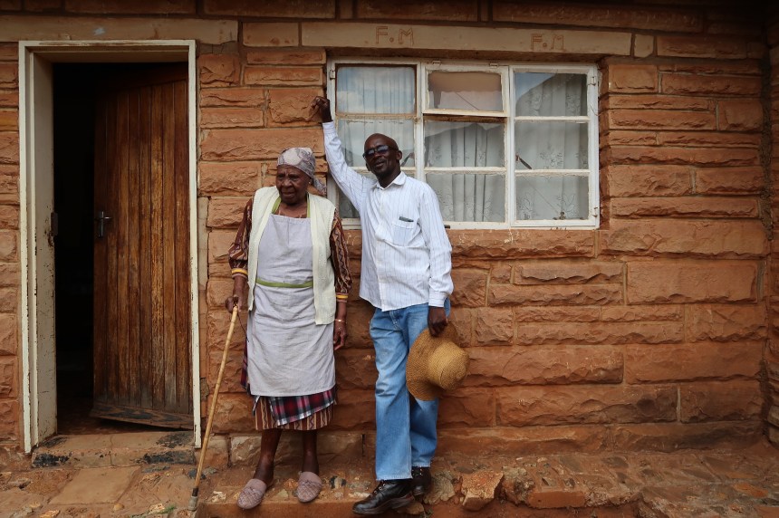 Albert Musi and his mother stand outside of the house his father built for them