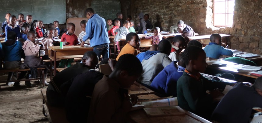 a crowd of student sitting at desks in a small, cramped rural classroom in Malealea, Lesotho