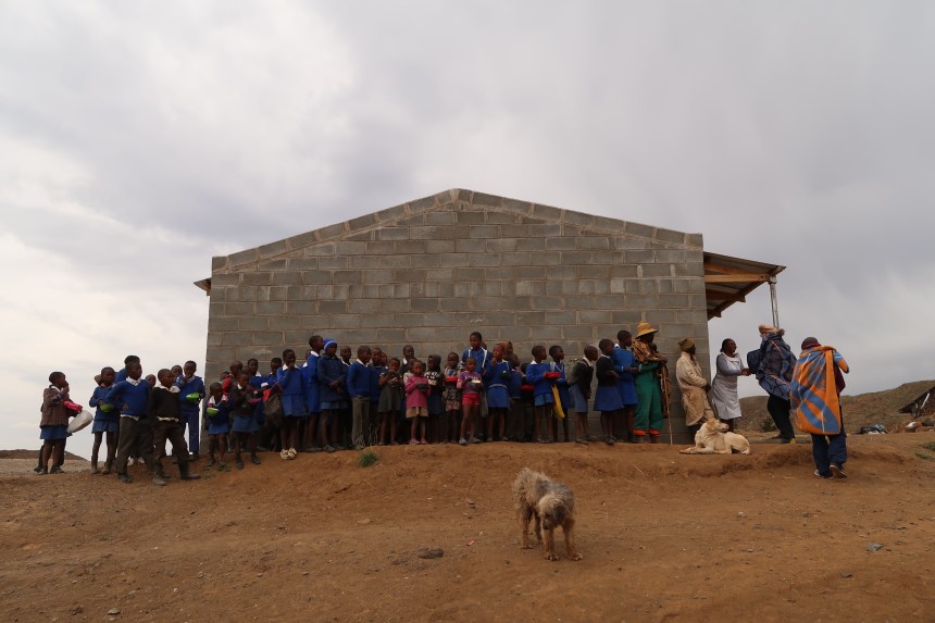 a group of children stand outside their school on a cloudy day in Malealea, Lesotho